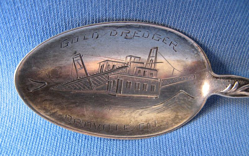 Souvenir Mining Spoon Bowl Gold Dredger Oroville CA.JPG - SOUVENIR MINING SPOON GOLD DREDGER OROVILLE CA - Sterling silver spoon with engraved bowl showing gold dredge and marked GOLD DREDGER OROVILLE CAL, top of handle shows California Poppy (state flower), 5 1/8 in. long, reverse marked Sterling (Oroville, CA is situated at the base of the foothills on the banks of the Feather River where it flows out of the Sierra Nevada onto the flat floor of the Sacramento Valley. It was established as the head of navigation on the Feather River to supply gold miners during the California Gold Rush.  The Feather River is one of the main river systems in California’s Mother Lode region. It is the major tributary to the Sacramento River, and was one of the first areas that gold was discovered during the gold rush in 1849.  Settled in 1849, Oroville originally was known as Ophir City, but the name was changed when the first post office opened in 1854.  Gold was discovered here at a site called Bidwell Bar, one of the earliest mining sites in California, bringing in thousands of miners.  The early miners worked the area by hand using shovels, picks, gold pans, and sluice boxes, and found the entire area to be exceptionally rich with gold dust and nuggets.  Around 1895, W. P. Hammon and others tested the area to determine the feasibility of mining on a large scale. They introduced bucket-line dredging in 1898, the first in California. The field was highly productive from 1903 to 1916; in 1908 there were 35 dredges and 12 dredging companies active in the field.  Output later declined, but dredging was done again from 1936 to 1942 and 1945 to 1952. The dredge field is now an important source of sand and gravel.  Throughout the history of dredging in California the Oroville district has floated more dredges and seen more dredging companies than any other areas in California.  Output from dredging in the Oroville area is estimated to be about 1,964,000 ounces of gold.)